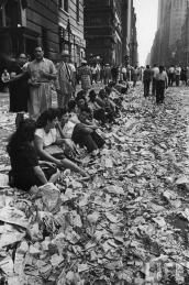 La gente si siede sul marciapiede tra i coriandoli del corteo che celebra la fine della seconda guerra mondiale. 14 ago 1945