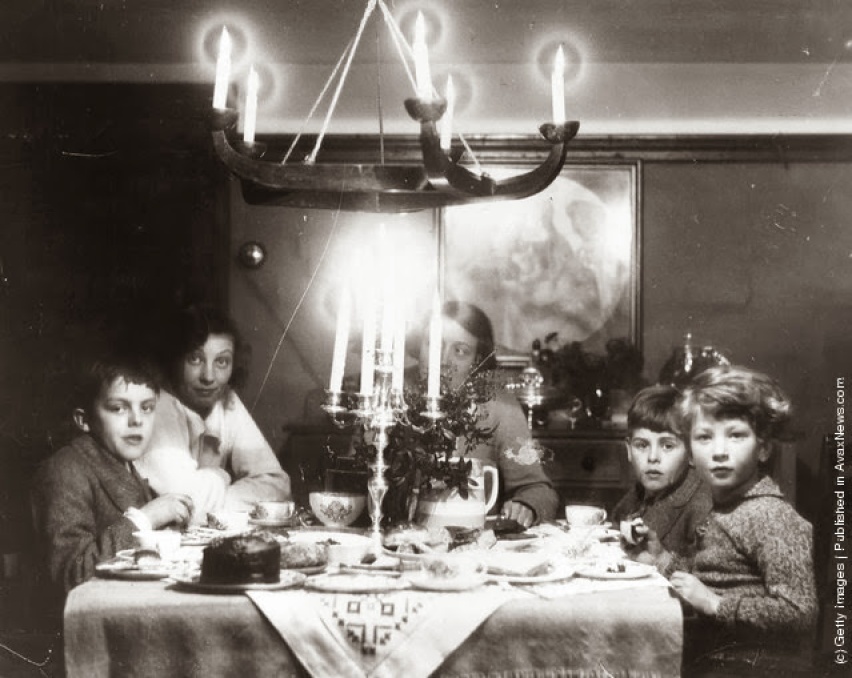 Una famiglia a Natale all'ora del tè con torta al cioccolato, un candelabro e agrifoglio sul tavolo. (Photo by Agenzia fotografica Generale: Getty Images). circa 1935
