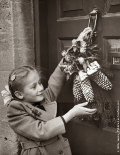 Una bambina appende una ghirlanda di Natale alla porta della sua casa a Northleach, Gloucestershire, in conformità con un vecchio costume locale. (Photo by Fox Foto: Getty Images). 24 dic 1954