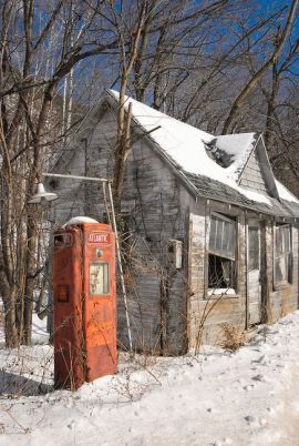 Stazione di servizio abbandonata nella neve e nella luce solare di inverno lungo il bordo della strada, americana rustica degli anni 60